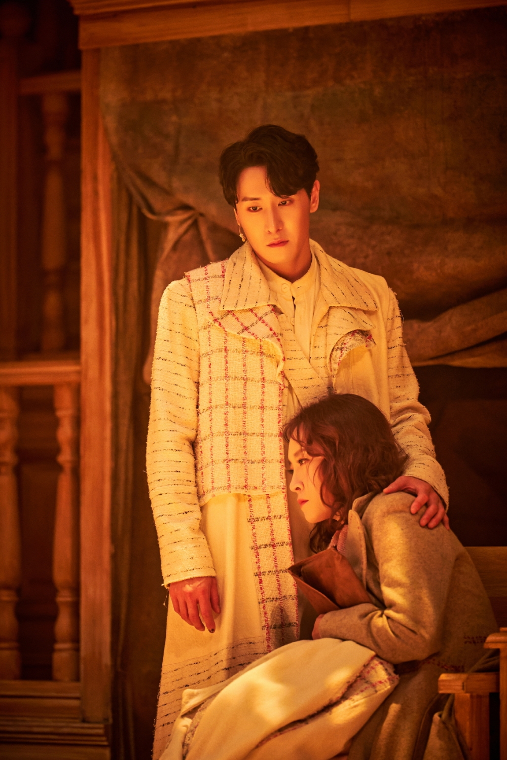 사진 설명 시작. 뮤지컬 「호프」의 2023년 공연 사진이다. 마리가 의자에 앉은 채 K에게 기대고 있다. 손에 원고를 쥔 상태다. K는 일어선 상태로 한 손으로 마리의 어깨를 잡고 있다. 두 인물의 표정은 모두 굳어 있다. 사진 설명 끝.