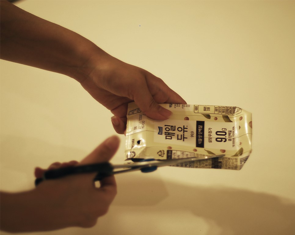 사진 설명 시작. 두유팩을 가위로 자르고 있다. 사진 설명 끝.