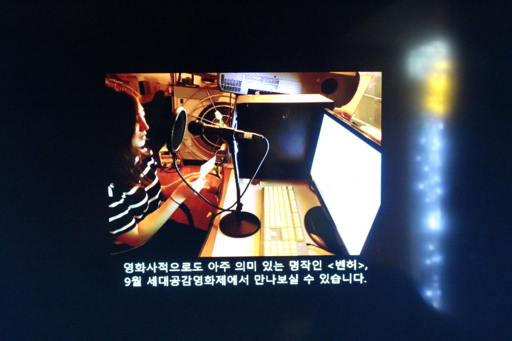 사진 설명 시작. 한 여성이 모니터를 앞에 둔 채 마이크에 대고 사연을 읽고 있다. 그 아래