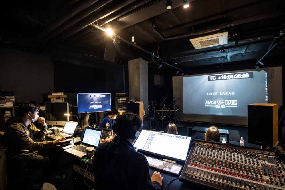 사진 설명 시작. 배리어프리영화 제작 현장이다. 중앙의 커다란 스크린이 있고, 제작자들이 콘솔 앞에 앉아 자막 삽입 작업을 하고 있다. 사진 설명 끝.