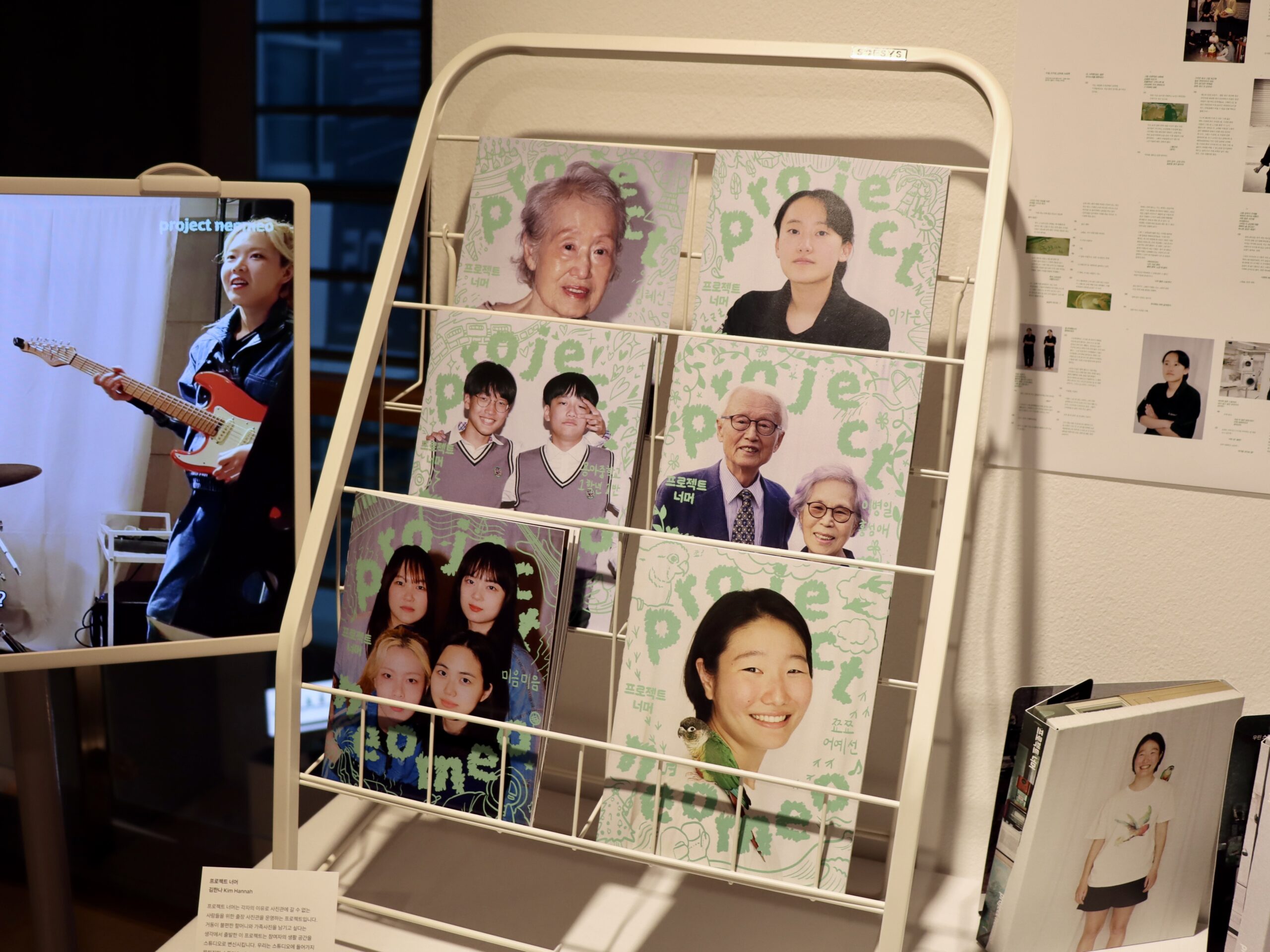 사진 설명 시작. 중앙에 6권의 잡지가 놓여 있고, 잡지 제목은 ‘project neomeo’이다. 잡지 표지에는 왼쪽 위편부터 할머니, 정장을 입은 사람, 교복을 입은 학생 두 명, 할머니와 할아버지, 캐주얼한 복장의 친구 네 명, 밝게 웃고 있는 단발의 사람 한 명의 사진이 있다. 왼편에는 모니터가, 오른편에는 다른 작품들이 놓여있고 오른쪽 뒤에는 작품 설명 포트폴리오가 비치돼 있다. 사진 설명 끝.